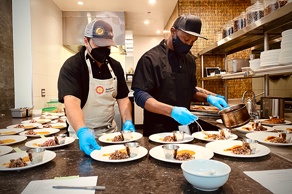 Two culinary apprentices prepare plates of food.